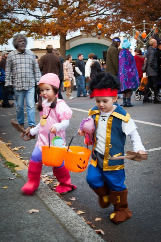 Children in colorful Halloween costumes holding plastic buckets at a public event.