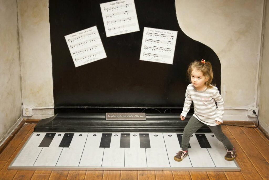A child stands on a floor art installation designed to look like the keys of a grand piano.