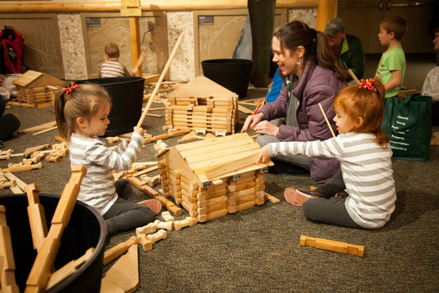 Imagine Children’s Museum Children participate in a woodworking activity, constructing small wooden structures with an instructor's guidance. Close-up view of the wooden building materials.