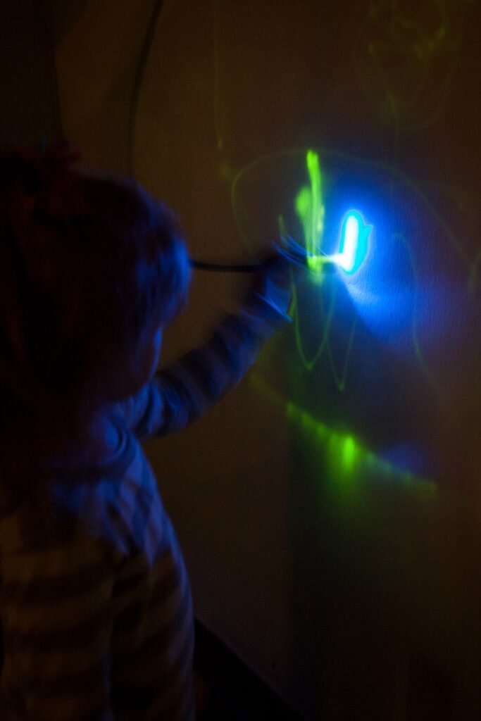 A child plays with blue and green glow paint in the dark, creating colorful light trails.