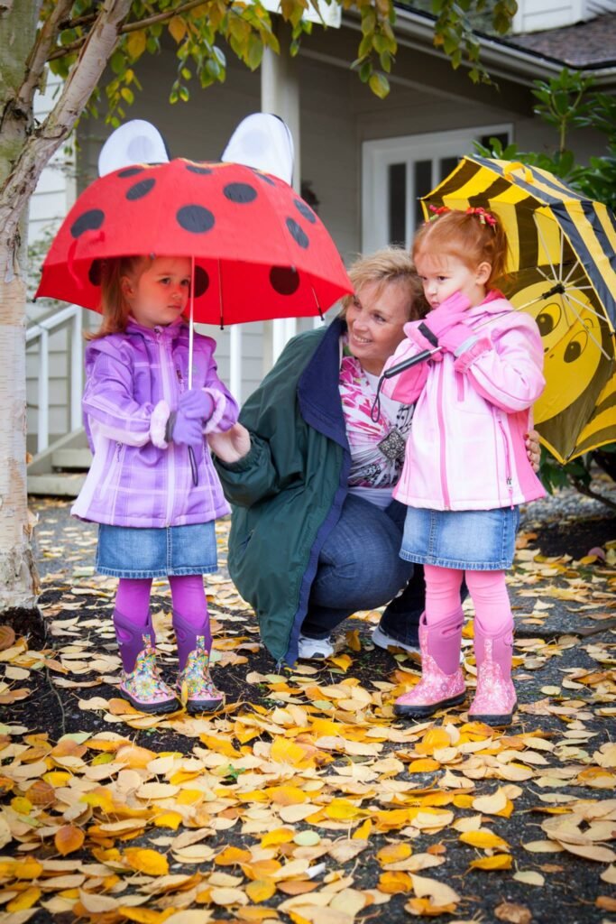 Children in colorful raincoats holding ladybug and bumblebee umbrellas on a leaf-covered path. A cozy autumn day outside in the Pacific Northwest.