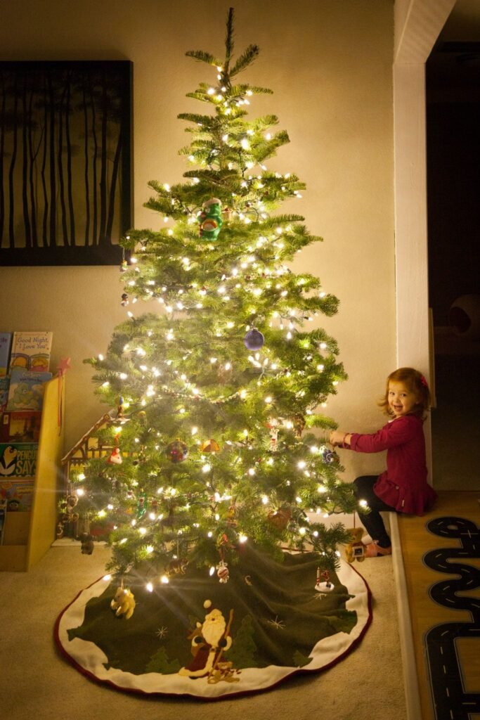 A child decorates a lit Christmas tree in a living room. Festive holiday scene with tree lights and ornaments.