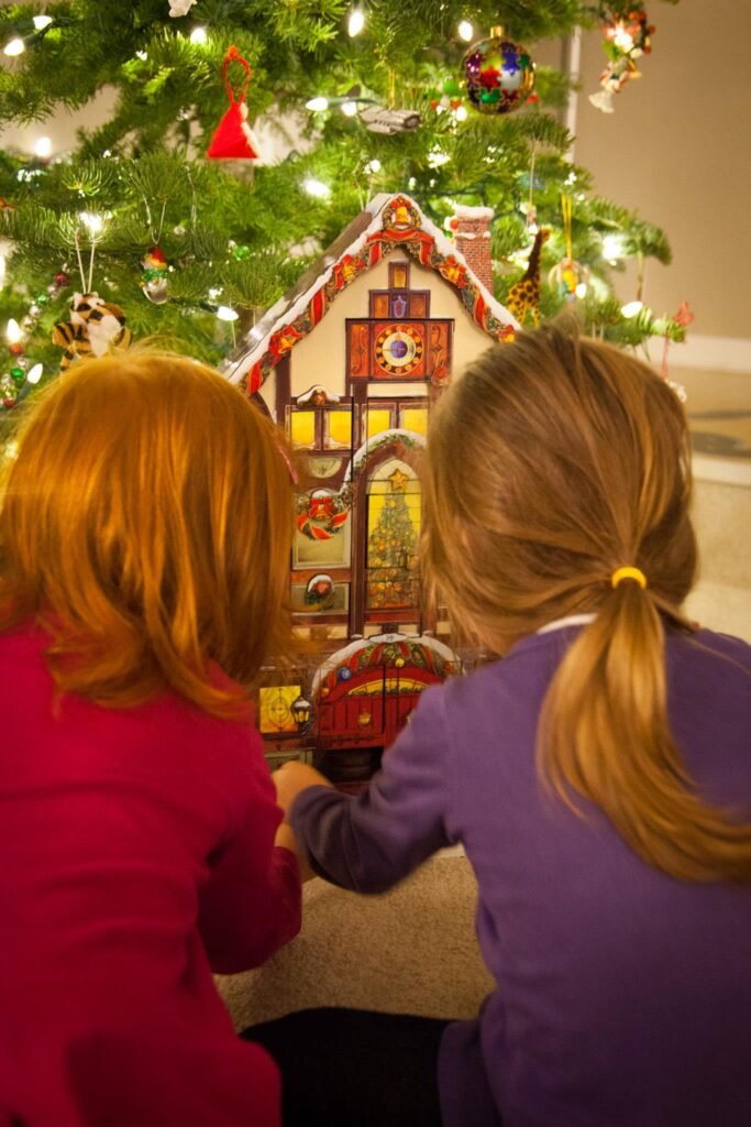 Two people enjoy a detailed gingerbread house beneath a glowing Christmas tree.