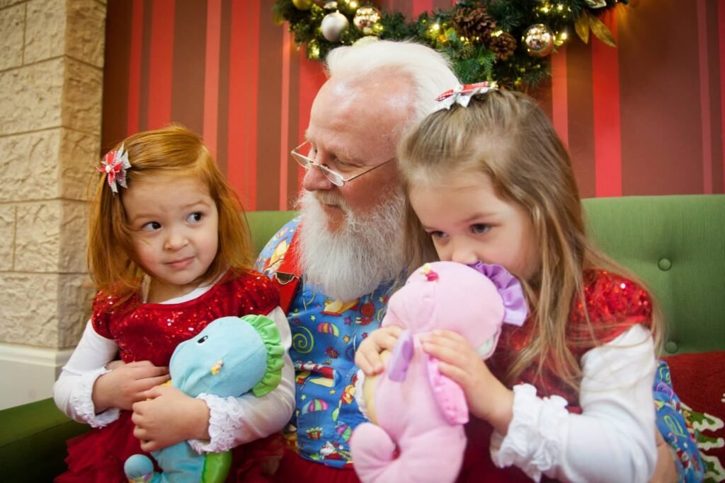 A cheerful visit with Santa Claus. Two young girls hold plush toys while Santa smiles warmly in a festive setting.
