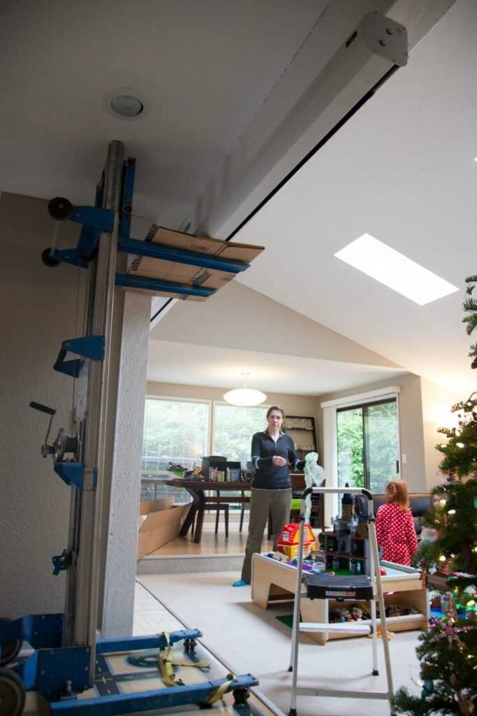 A woodworking project in progress in a bright living room with a ladder, tools, and a Christmas tree.