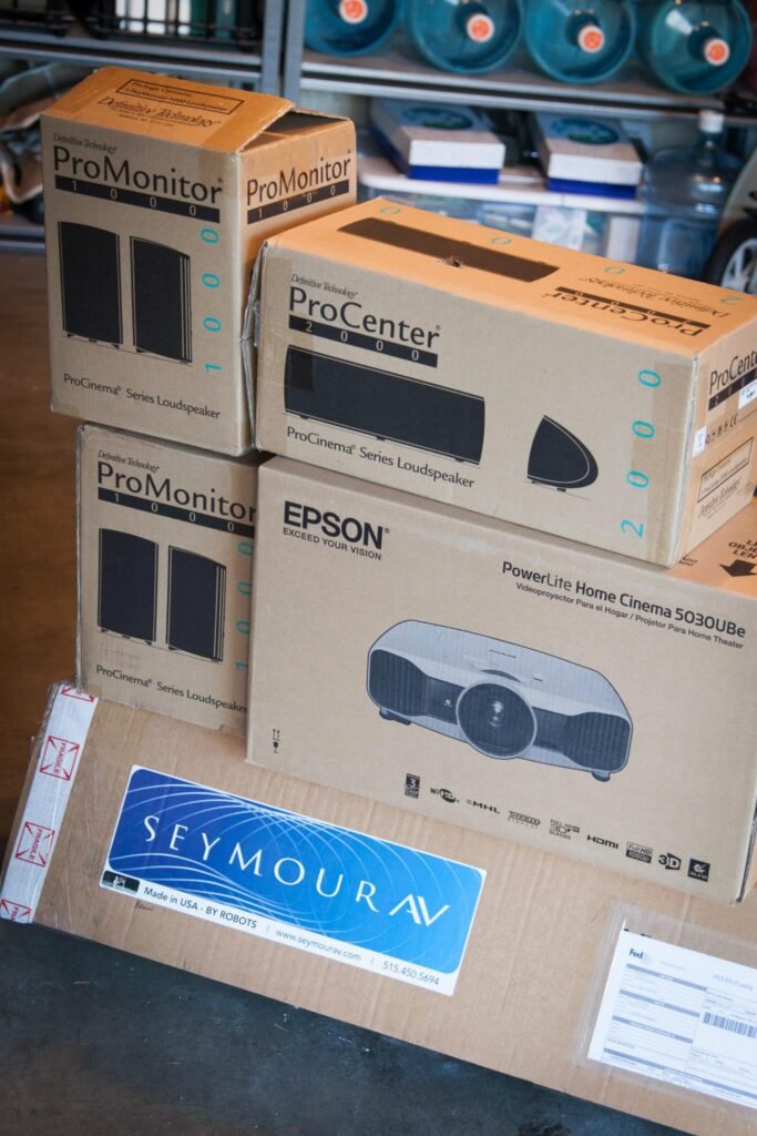Stacks of ProMonitor and Epson projector boxes on a table.