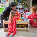 A family enjoys playing with toys and presents on Christmas morning. The children wear matching red pajamas with white polka dots.
