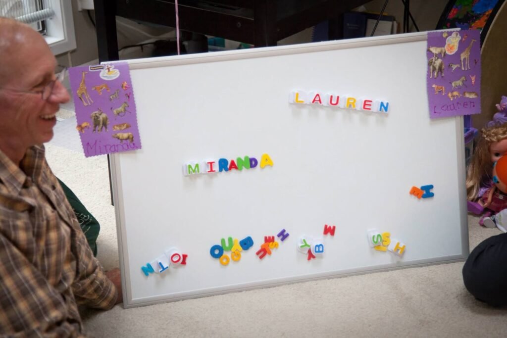 A person smiling while spelling out playful phrases with colorful magnetic letters on a whiteboard.