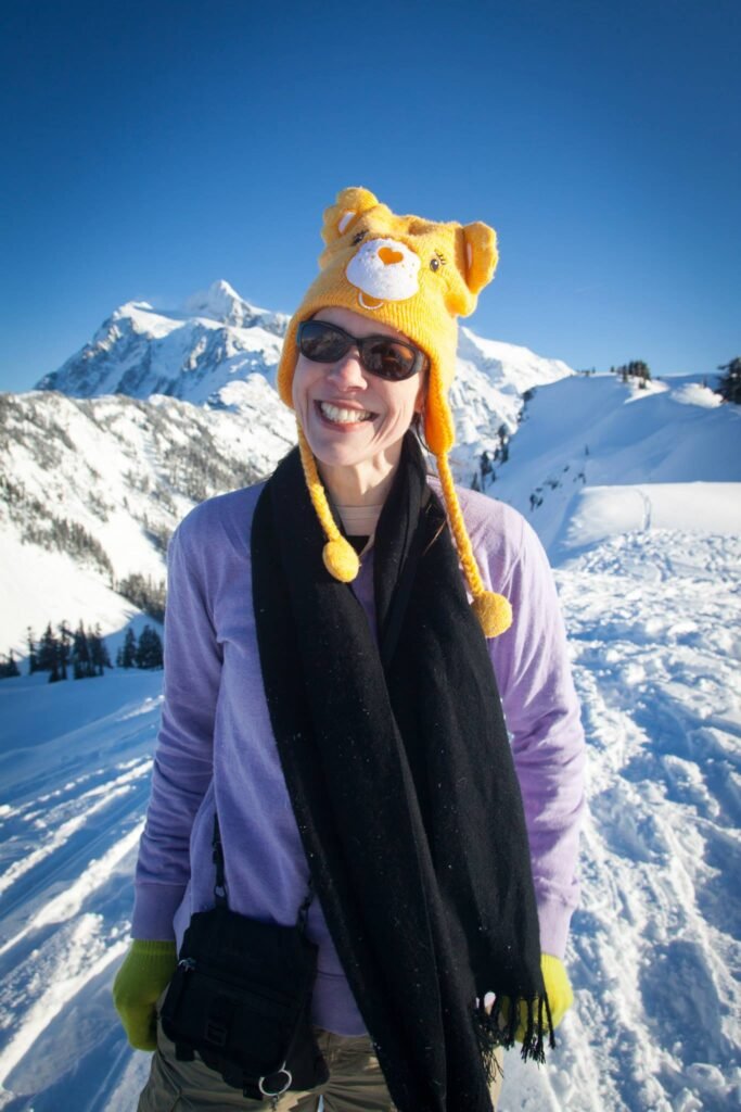 A person wearing a Tigger-themed hat and sunglasses stands on a snowy mountain slope.