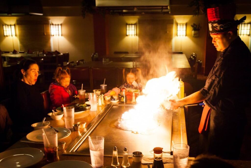 A chef performs a flambé cooking demonstration in front of a group of diners.