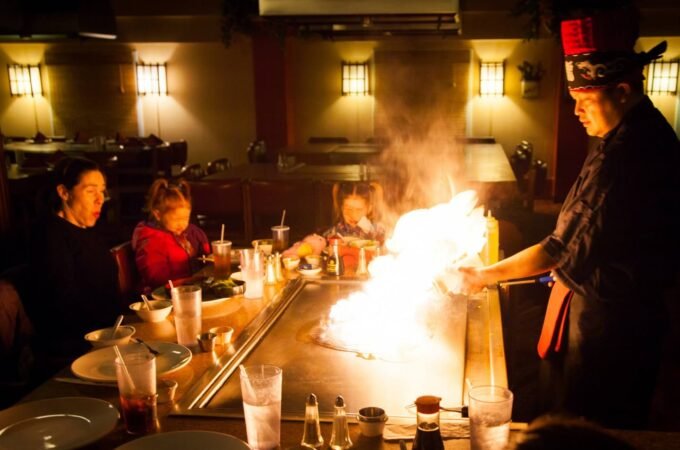 A chef performs a flambé cooking demonstration in front of a group of diners.