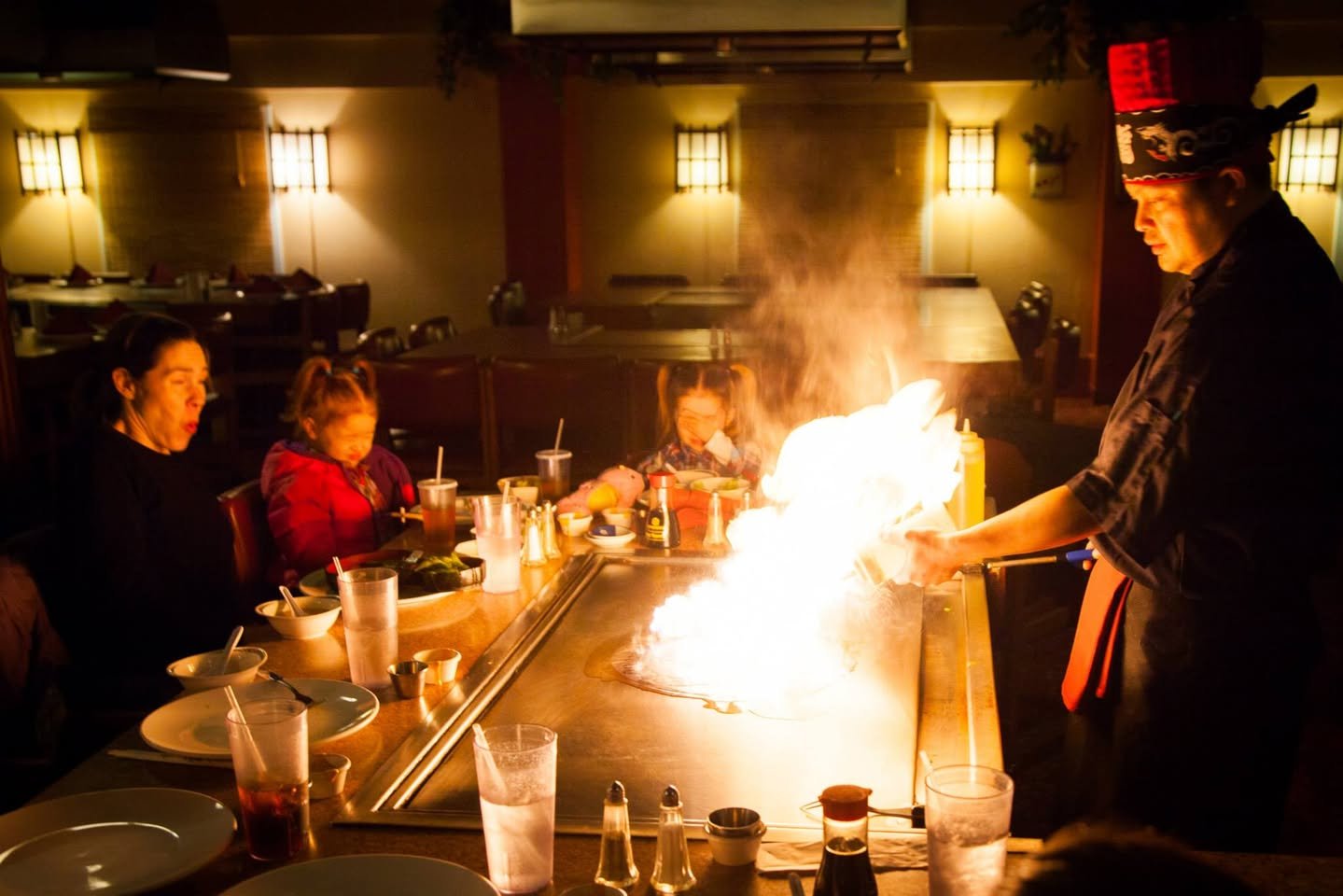A chef performs a flambé cooking demonstration in front of a group of diners.