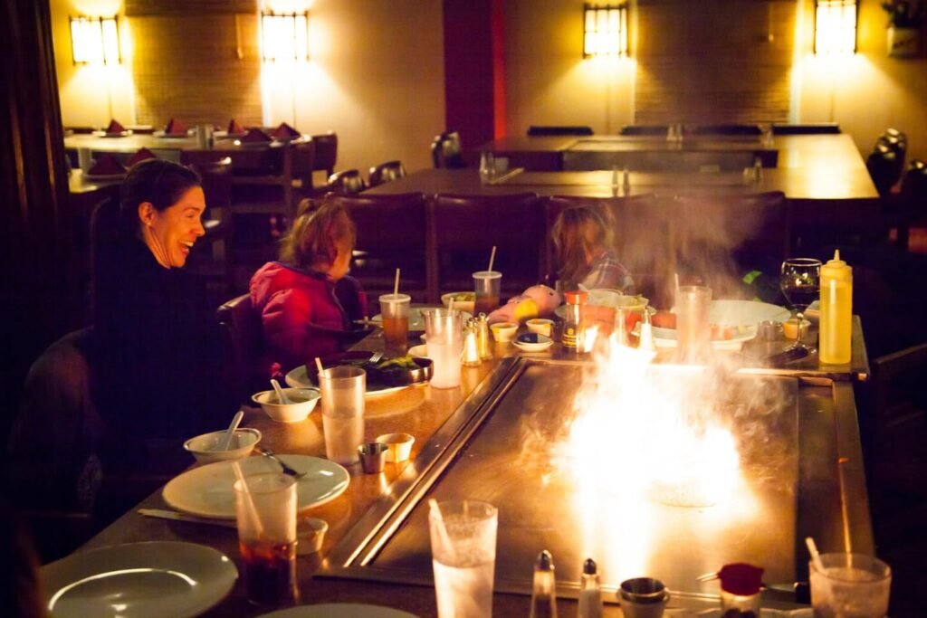A chef performs a flaming dish at a teppanyaki grill in a warmly lit restaurant.