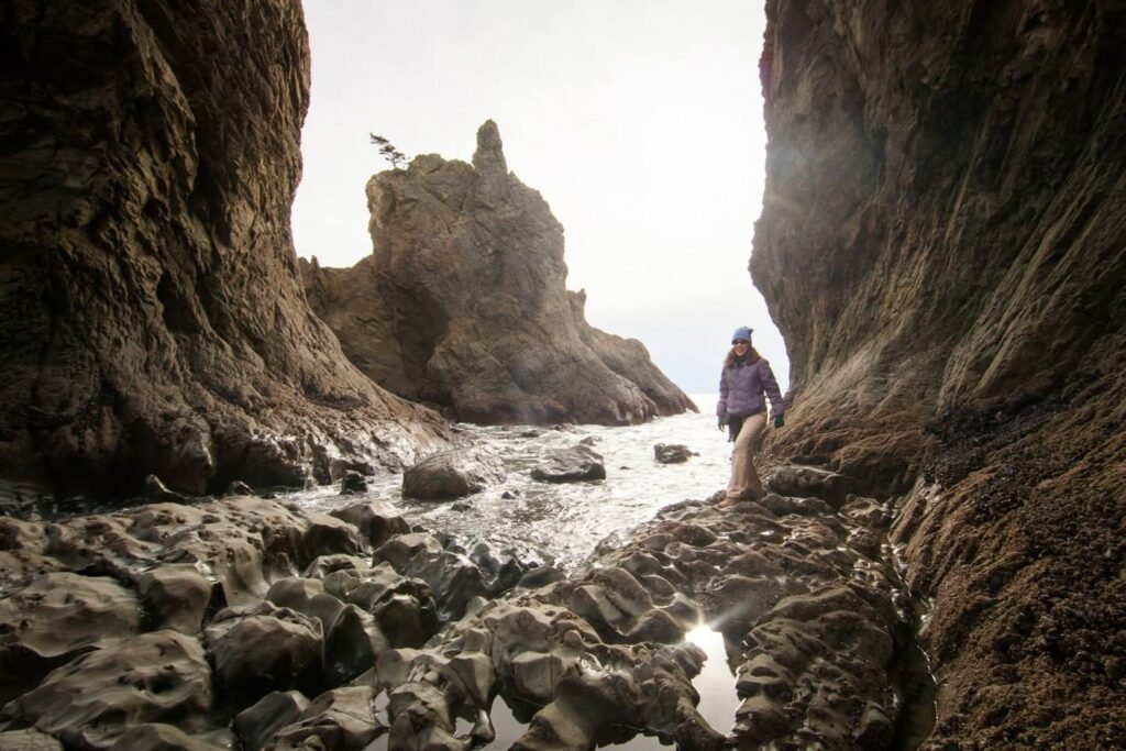 A muddy coastal scene showing tide pools between rocky walls, with a distant view of bold sea stacks.