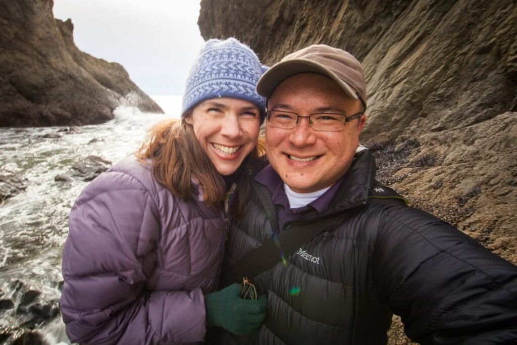 A couple enjoying a sunny day at rugged coastal cliffs, bundled up in winter hats and jackets.