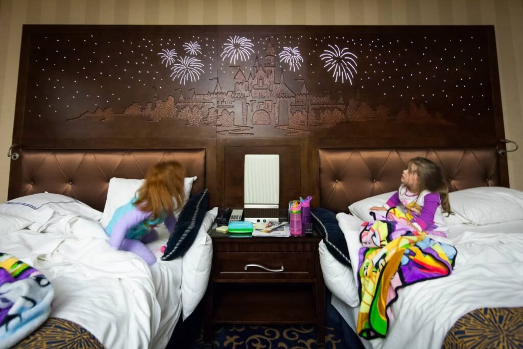 A hotel guest room with twin beds and a unique wall mural depicting fireworks. Children are relaxing in the beds under colorful blankets.