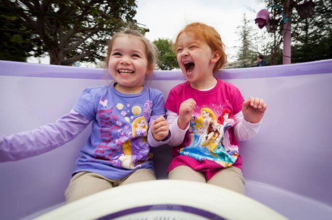 Two children enjoying a spinning ride at an outdoor amusement park, captured from multiple angles with joyful expressions.