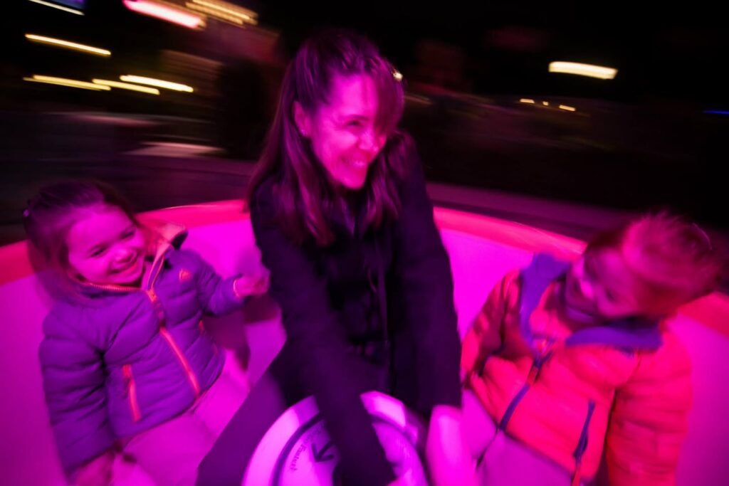 Three people smiling on a glowing pink float at a nighttime attraction.