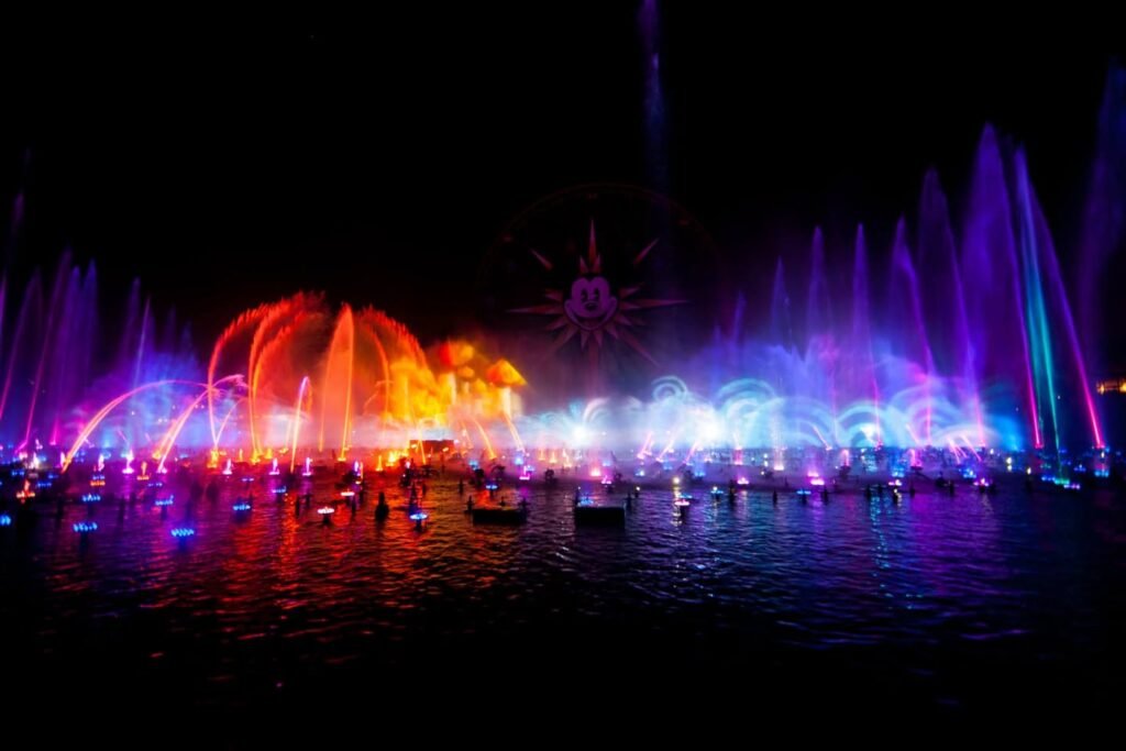 A stunning nighttime fountain show featuring vibrant purple, blue, and orange lights dancing across the water surface.