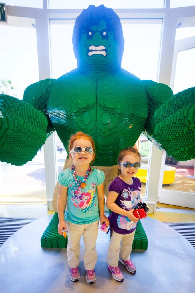 Two children standing in front of a large LEGO Hulk sculpture at a museum.