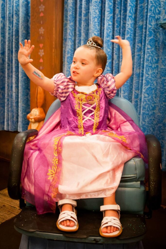 A young child models a pink and purple princess dress with a tiara.