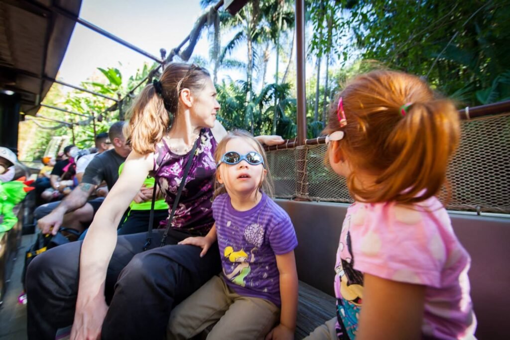 Travelers sit on an open-sided vehicle surrounding lush palm trees and dense jungle vegetation.