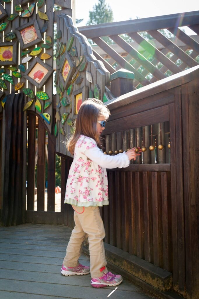 A child explores a handcrafted garden gate with decorative tile accents and a stained-glass-like column detail.