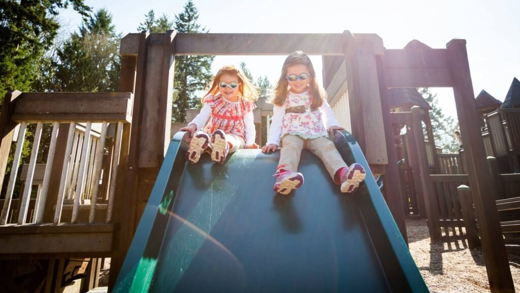 Children playing on a wooden playground slide on a sunny day.