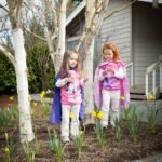 Moab Two children in colorful costumes standing among blooming daffodils and young trees in a Pacific Northwest garden.