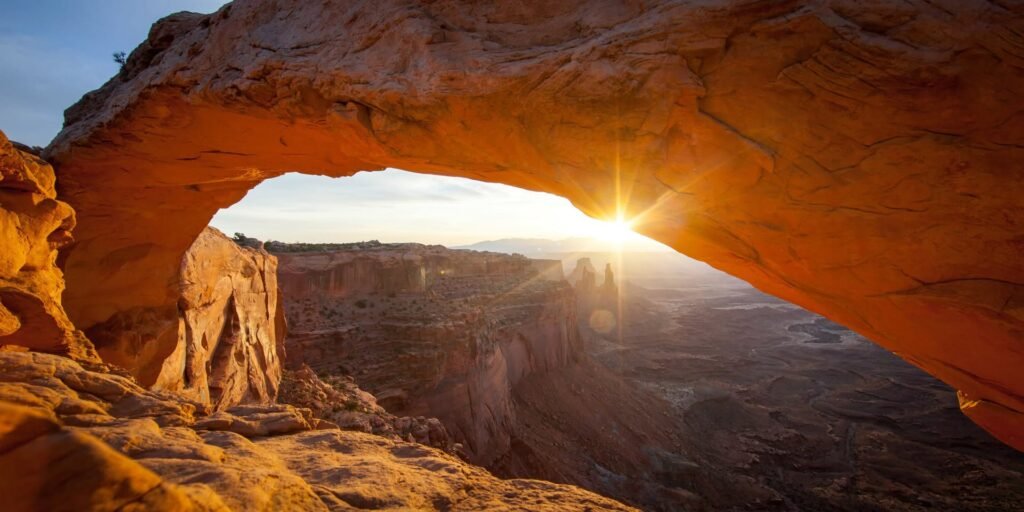 A stunning view of a natural rock arch glowing with golden light at sunset, seamlessly framed against a rugged desert landscape.