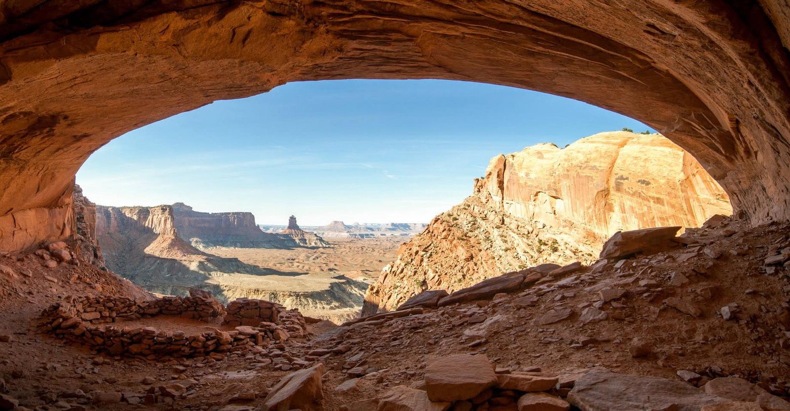 Moab A scenic panoramic view of desert cliffs and rocky terrain seen through an open natural arch.