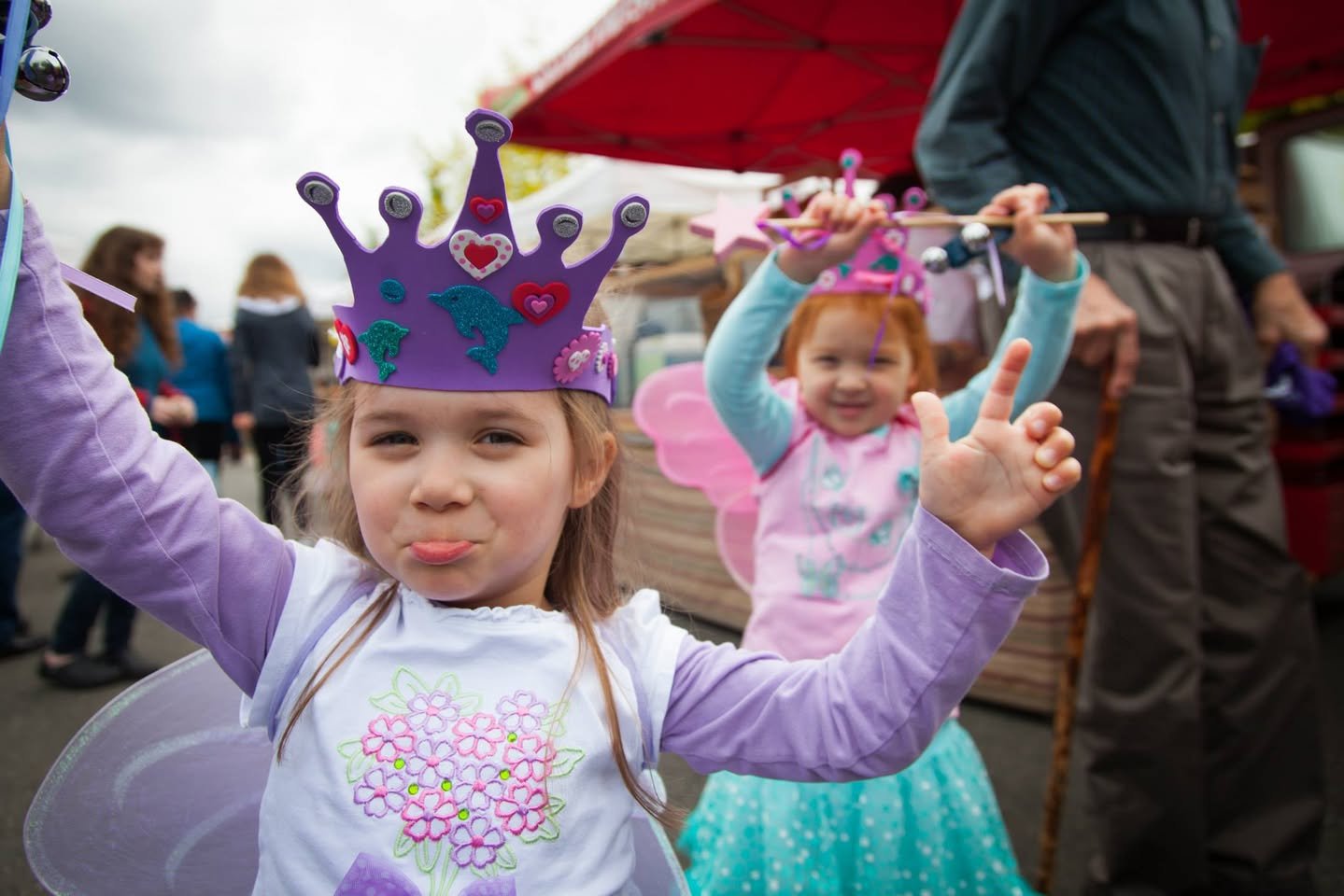 Children wearing purple and pink princess crowns pose joyfully at a theme park event. One child strikes a playful pose while another smiles brightly in the background.