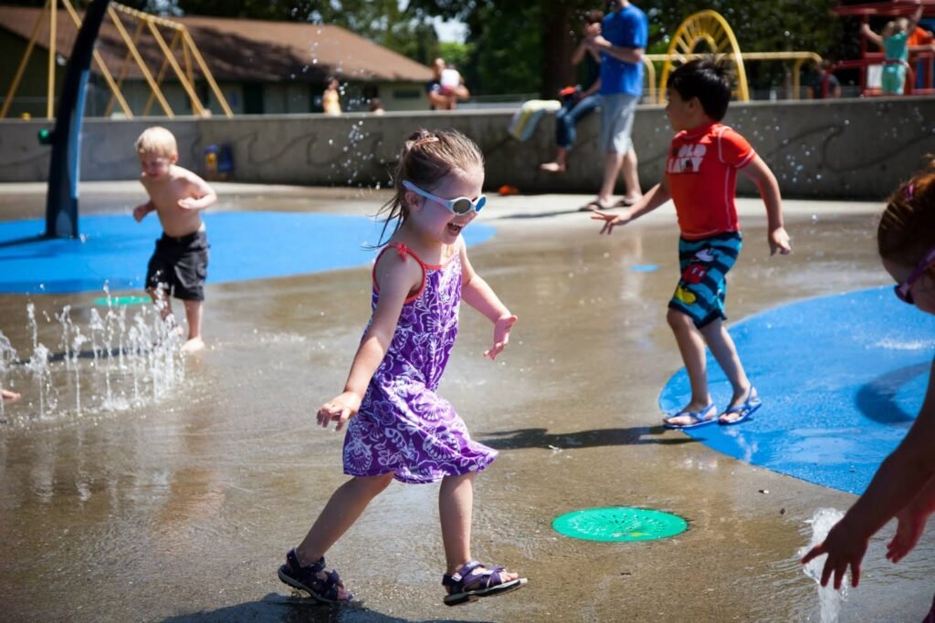Children playing and splashing in the water at an outdoor park on a sunny summer day.