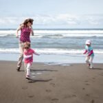 Adults and children playing on a sandy beach with ocean waves in the background.