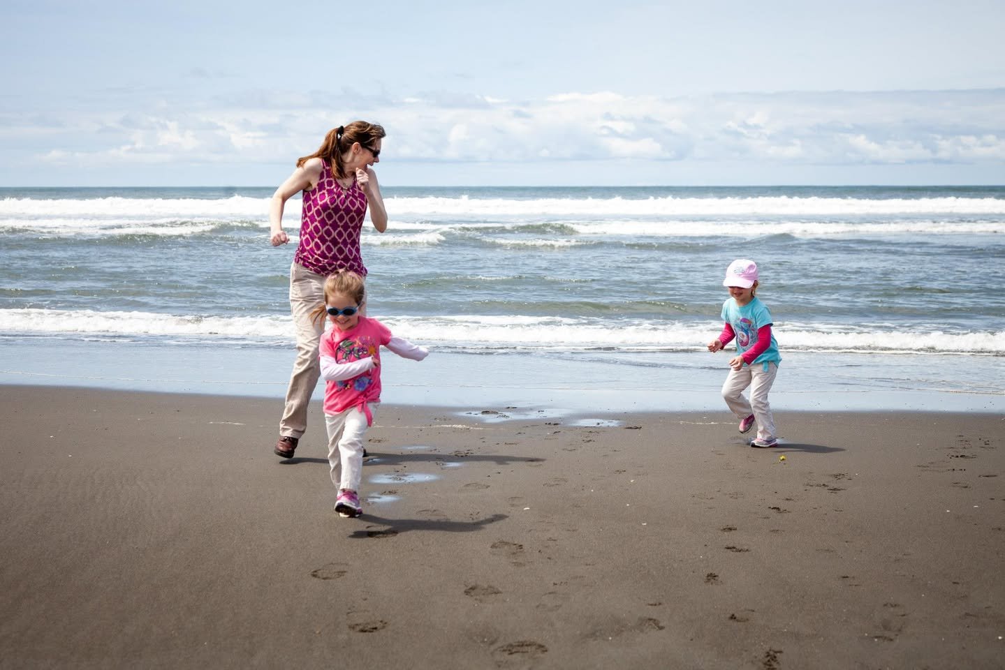 Adults and children playing on a sandy beach with ocean waves in the background.