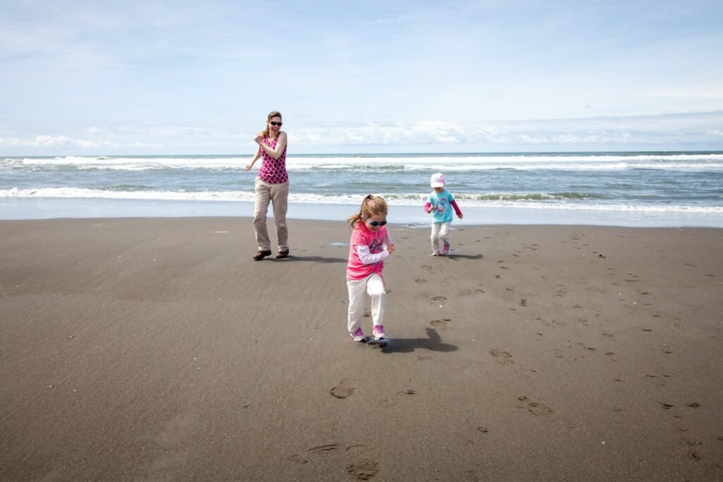 A family enjoys a sunny day walking along a wide, sandy beach near the shoreline. Gentle waves and a clear sky complete the tranquil coastal scene.