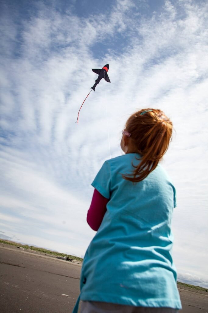 A person looks up at a jet-shaped kite flying high in a bright, partly cloudy sky.