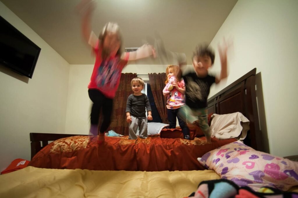 Kids bouncing energetically on a bed in a cozy bedroom.