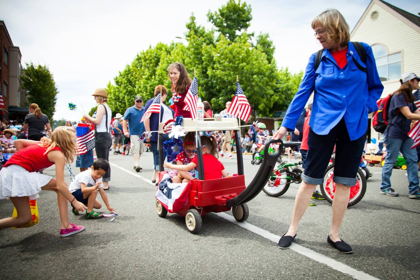 Spectators watch a red flag-decorated wagon in a community parade on a sunny street.