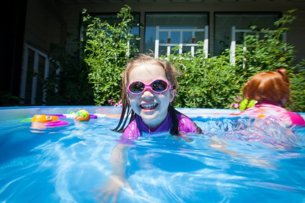 Children splash in a bright blue above-ground pool, surrounded by lush greenery and colorful toys.