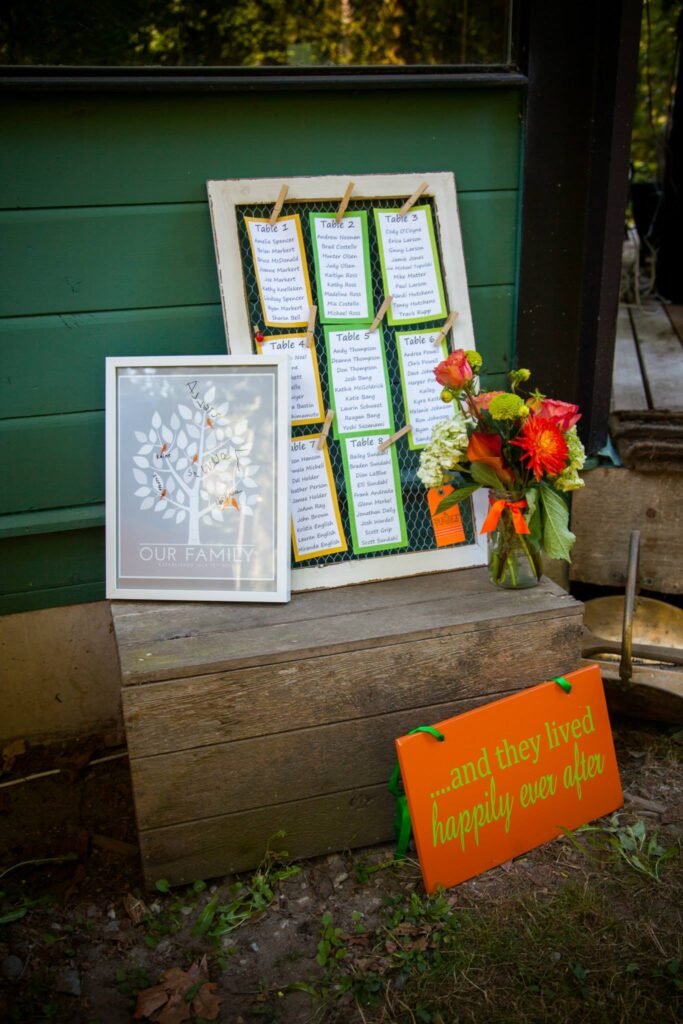 A rustic display of wedding scripts in frames on a wooden crate, beside a framed tree design and a vibrant floral bouquet.