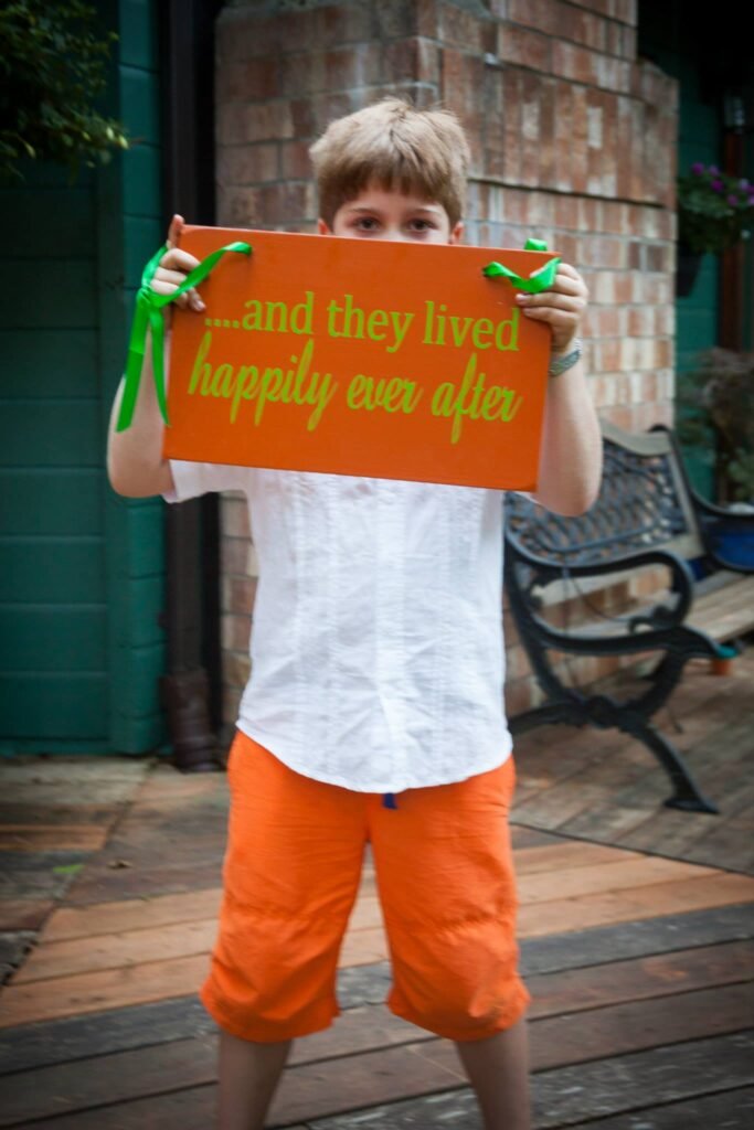 A young individual holds a sign reading 'and they lived happily ever after' on a wooden deck.