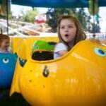 Children in colorful fish-shaped amusement rides enjoy a whimsical day at the fairground. Brightly painted yellow and blue fish add a playful touch.