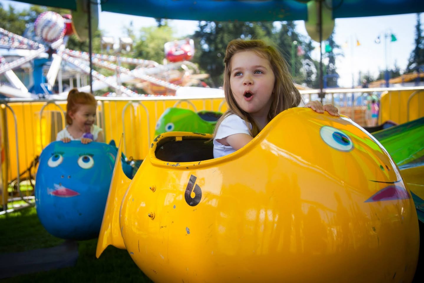 Tour de Terrace Fair Children in colorful fish-shaped amusement rides enjoy a whimsical day at the fairground. Brightly painted yellow and blue fish add a playful touch.
