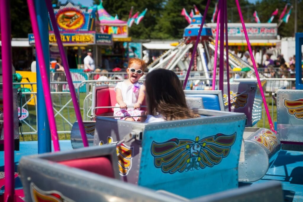 A family enjoying a colorful carnival ride with summer fun at a North American fairground. Sunny day atmosphere with bright pink poles and festive decorations.