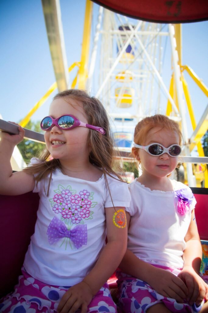 Two children wearing sunglasses enjoying a ride on a yellow Ferris wheel against a clear blue sky.