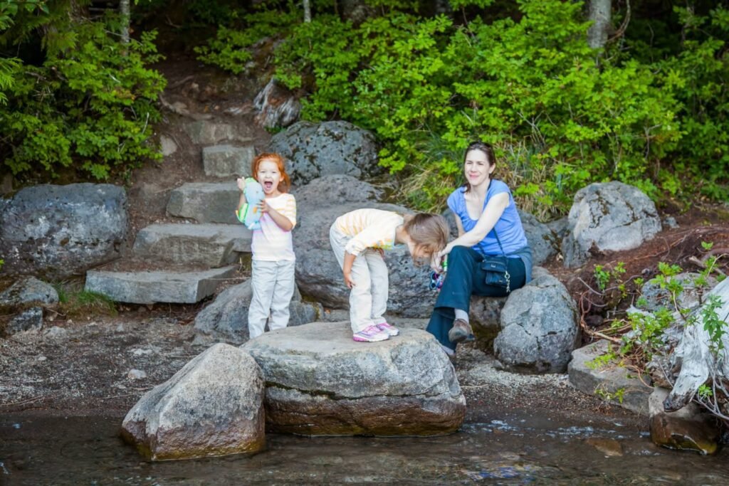 Individuals enjoy a rocky creek area with stone steps and lush green vegetation. A family enjoys a nature walk on a rock-filled trail.