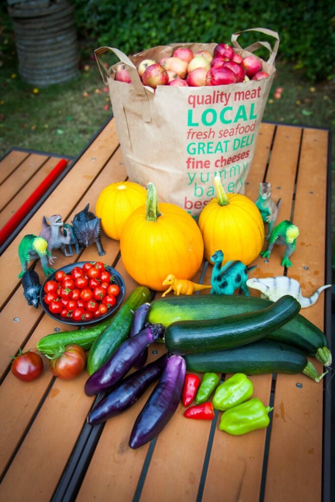 A colorful assortment of fresh vegetables and fruits, including squash, eggs, cucumbers, and peppers, displayed on a wooden table.