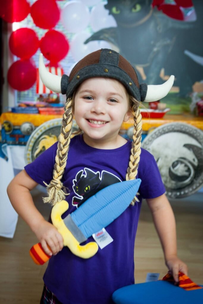 A child in a detailed Viking costume including a horned helmet and braided hair, holding a toy sword.