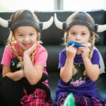 Iceland Two children wearing Viking-style horned helmets are posing on a black leather couch.
